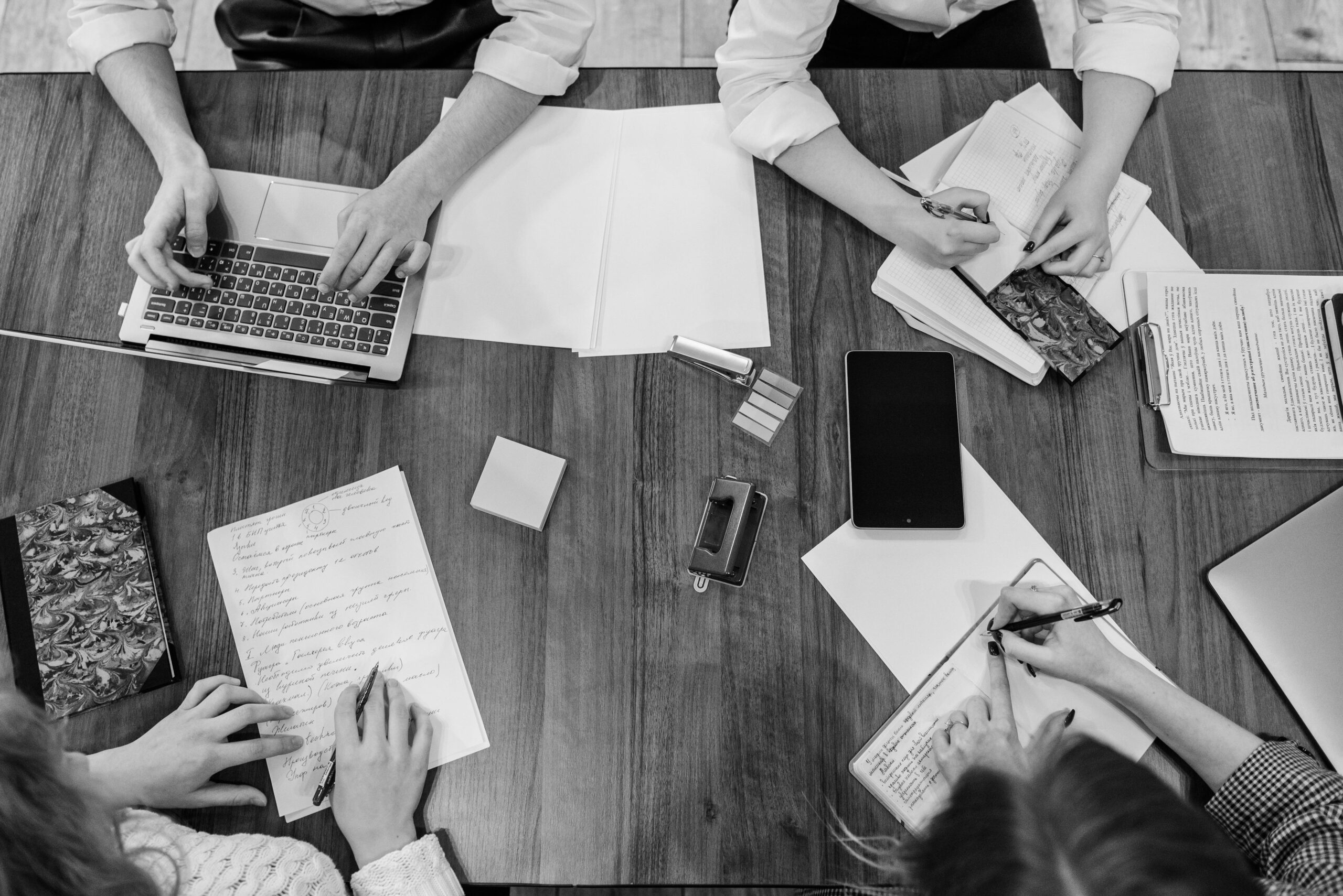 Top view of team members working together on a wooden table, using various office tools.